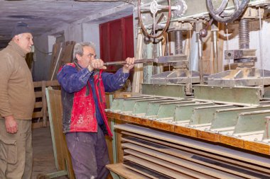 İşçiler makineyi sıkıştırıyor, metal manivelayla mekanizmayı çeviriyor. Marangozlukta ahşap profillerin elle üretimindeki kurutma tutkalı süreci