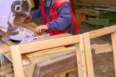 Marangoz el testeresinin kalaslarını kesti ve marangozluk atölyesindeki bir mezura kullanarak uzunluğunu kontrol etti..