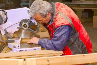 Marangoz çalışır, el testeresinde kalas keser, marangozluk atölyesinde ahşap işçiliği yapar.. 