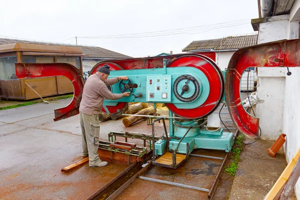 Worker at the outdoor carpentry regulate large industrial band saw for wood processing.