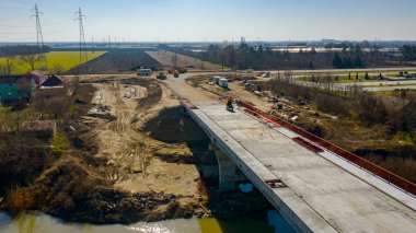 Güneş ışığı yukarıdan görünüyor, bitmemiş beton köprü, inşaat halindeki nehir üzerindeki yol, inşaat alanı..