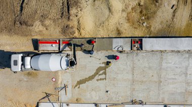 Üst manzarada, inşaat işçilerinin genel giderleri tırmıkla yayılıyor ve mikser kamyonundan dökülen taze betonu kare siperlere yerleştirmek için metal katman kullanılıyor..