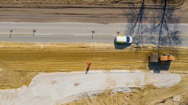 Tepede, üzerinde çiviler olan dev bir yol silindiri var. Toprak sıkıştırıyor, inşaat sahasında kum var. Aktif trafik temeline yakın bir yerde..