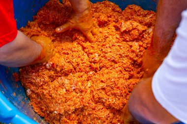 Erkekler, et parçalarını derin bir plastik kasede karıştırmak için birlikte çalışıyorlar. Sosis yapmak için açık havada et işliyorlar..