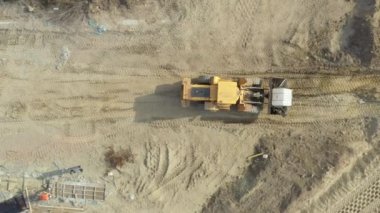 En üstte, tepedeki bebek hareket halinde, inşaat alanının üzerindeki kovasında plastik rezervuar taşıyan tekerlekleri olan buldozer üzerinde..