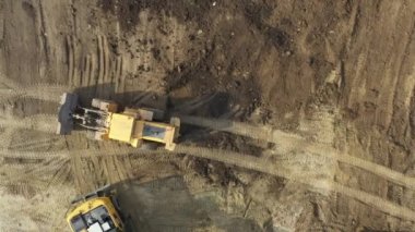 Tepe manzaralı, tepedeki doli hareket ediyor. Tekerlekli buldozer inşaat alanının üzerinden geçiyor. Kovasını kullanarak zemini düzleştiriyor..