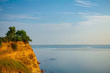 Huzurlu körfezin üzerinde bitki örtüsü ve deniz kabuğu çiftliği olan kayalık açık denize yerleştirilir..