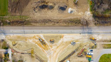 Üstten, tepeden, dairesel yolda, inşaat halindeki döner kavşak, inşaat alanındaki işçilerden oluşan ekip ağır makinelerle yol temeli üzerinde çalışıyor..