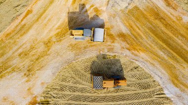 Tepede, tepede, iki yol silindirinde, dikenli kumu sıkıştıran düz olan yeni trafik kavşağı tabanı için çakılları düzleştiriyor..