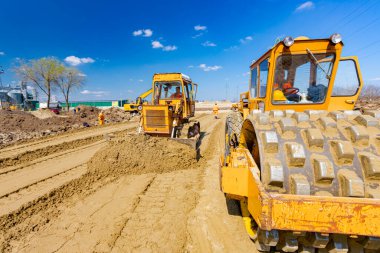 Dikenli ve buldozerli yol silindiri, inşaat alanındaki yol temeli için kum seviyesini düşürüyor..