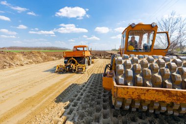 Çivili yol silindiri ve plaka titreşim sıkıştırıcılı kamyon inşaat alanındaki yol temeli için kumu düzleştiriyor..