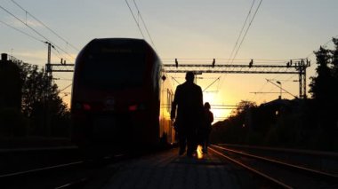 Yolcu treni tren istasyonuna vardı, insanlar aceleyle yürüyordu, güneş arka plandaydı. Siluet, insanların gölgeleri, yolcular, banliyö yolcuları iş hayatında trenden iniyorlar, yoğun yaşam tarzı ulaşımı.