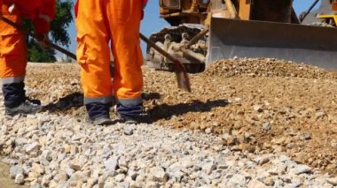 Zrenjanin, Voyvodina, Sırbistan - 21 Nisan 2021: İnşaat alanındaki küçük ezilmiş taş tabakası, kesir tabakasını düzleştiren doğru ölçümlere temel oluşturmak için kürek kullanan iki işçiye düşük açılı bakış.