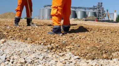 Zrenjanin, Voyvodina, Sırbistan - 21 Nisan 2021: İnşaat alanındaki küçük ezilmiş taş tabakası, kesir tabakasını düzleştiren doğru ölçümlere temel oluşturmak için kürek kullanan iki işçiye düşük açılı bakış.