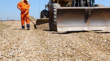 Zrenjanin, Voyvodina, Sırbistan - 21 Nisan 2021: İşçiye düşük açılı bakış açısı, inşaattaki küçük ezilmiş taş tabakasını düzleştirene kadar, kademe bıçağının kesirini itmek için kürek kullanıyor.