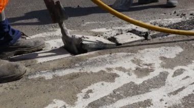 İnşaat işçisi pnömatik bir matkapla asfaltı kırıyor. Kırık parçaları toplayıp atmak için kürek kullanan bir adam..
