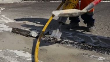 İnşaat işçisi pnömatik bir matkapla asfaltı kırıyor. Kırık parçaları toplayıp atmak için kürek kullanan bir adam..