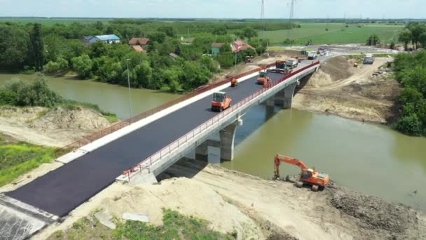 在工人和铺设沥青路面的机械上 在未完工的桥上铺一层热跑道 在河上修路 在建筑工地 — 图库视频影像