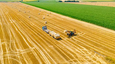 Kazıcının üzerinde, karavana saman balyaları yüklerken, tarla arazisinde, forklift bıçağı kullanarak, ek taşıyıcı.