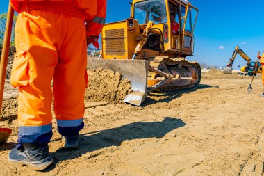 İşçiler ayakta durup tırtıllı toprak taşıyıcının dışarıda dünyayı hareket ettirmesini izliyor..