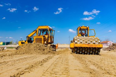 Dikenli ve buldozerli yol silindiri, inşaat alanındaki yol temeli için kum seviyesini düşürüyor..