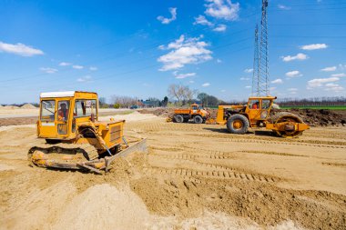 Çivili yol silindiri, buldozer ve kamyon plaka sıkıştırıcı ile sıkıştırılıyor, inşaat alanındaki yol temeli için kumu düzleştiriyor.