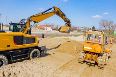 İnşaat alanındaki yol temeli için kum seviyesini ayarlayan buldozer ve kazıcıya arkadan bak, mekanizasyon.