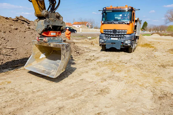An excavator pulls a tipper truck with a cord to help him to get out from sand at building site.