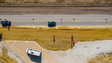 Üst manzara, yuvarlak yol, inşaat halindeki döner kavşak, inşaat alanındaki işçilerden oluşan ekip aktif trafiğin yanındaki yol temeli üzerinde çalışıyor..