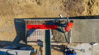 Üst manzarada, inşaat işçilerinin genel giderleri, mikser kamyonundan dökülen metalle yeni betonu kareye sabitliyor..