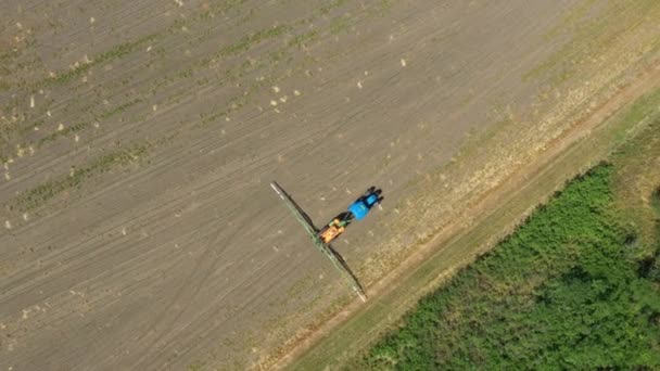 上から見ると 広大な農地を耕すまでトラクターの上から俯瞰し 草原の上に広い農業用噴霧器を設置する — ストック動画