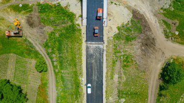 Tepede, tepede, birkaç buharlı silindirde taze asfaltı düzleştirirken, hazır zemin üzerine sıcak asfalt tabakası yayılıyor..