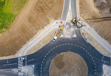 Üst manzara, yuvarlak yol, inşaat halindeki döner kavşak, inşaat alanındaki işçilerden oluşan ekip aktif trafiğin yanındaki yol temeli üzerinde çalışıyor..