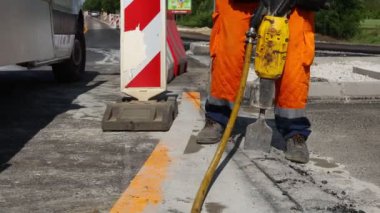 İnşaat işçisi pnömatik bir matkapla asfaltı kırıyor. Kırık parçaları toplayıp atmak için kürek kullanan bir adam..