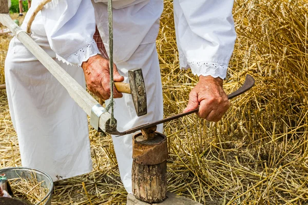 Bauer schärft, bügelt, repariert die Klinge an der Sense. — Stockfoto