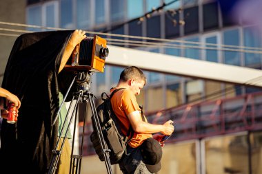Belgrade, Serbia - June 28, 2025: Photographer is taking photo of people, using old vintage retro camera, made of wood and metal, wooden box design, on modern professional tripod at public event.