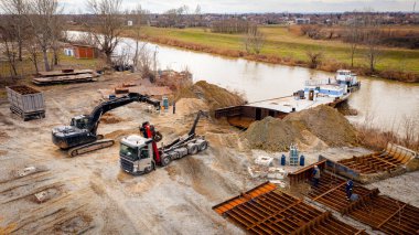 Manzaralı kazıcı ve çekicinin üstünde birlikte eski yük gemisinin yatağının bir kısmını çekiyorlar, mavna, nehir kıyısı, kazma, sökme gemisi, paslı metali kesme, geri dönüşüm....