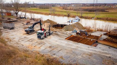 Manzaralı kazıcı ve çekicinin üstünde birlikte eski yük gemisinin yatağının bir kısmını çekiyorlar, mavna, nehir kıyısı, kazma, sökme gemisi, paslı metali kesme, geri dönüşüm....