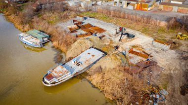 Manzaralı kazıcı ve çekicinin üstünde birlikte eski yük gemisinin yatağının bir kısmını çekiyorlar, mavna, nehir kıyısı, kazma, sökme gemisi, paslı metali kesme, geri dönüşüm....