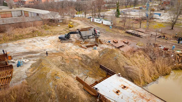 Above view on excavator and tow grapple truck with hydraulic grappling claw, multivalve grab hand, gripper machine, manipulator, loading part of vessel into container, collect rusty metal, recycling.