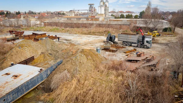 Above view on excavator and tow grapple truck with hydraulic grappling claw, multivalve grab hand, gripper machine, manipulator, loading part of vessel into container, collect rusty metal, recycling.