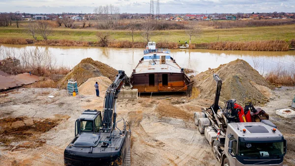 Manzaralı kazıcı ve çekicinin üstünde birlikte eski yük gemisinin yatağının bir kısmını çekiyorlar, mavna, nehir kıyısı, kazma, sökme gemisi, paslı metali kesme, geri dönüşüm....