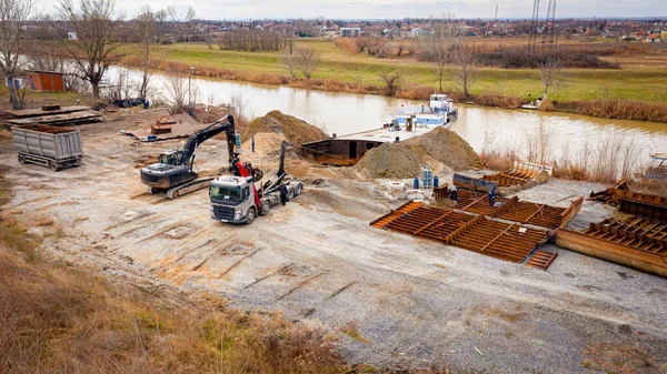 Manzaralı kazıcı ve çekicinin üstünde birlikte eski yük gemisinin yatağının bir kısmını çekiyorlar, mavna, nehir kıyısı, kazma, sökme gemisi, paslı metali kesme, geri dönüşüm....