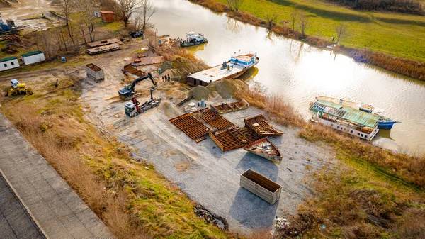 Manzaralı kazıcı ve çekicinin üstünde birlikte eski yük gemisinin yatağının bir kısmını çekiyorlar, mavna, nehir kıyısı, kazma, sökme gemisi, paslı metali kesme, geri dönüşüm....