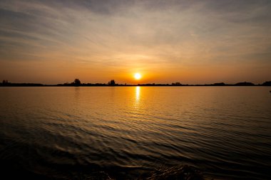 Akşamları güzel günbatımının manzarası gölün üzerinde, gölün üzerinde siluet suyun üzerinde ve bulutların sakin sularda yansıması.