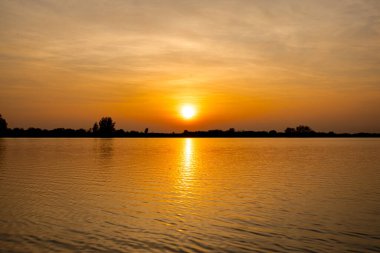Akşamları güzel günbatımının manzarası gölün üzerinde, gölün üzerinde siluet suyun üzerinde ve bulutların sakin sularda yansıması.