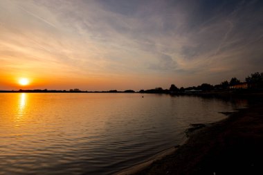 Akşamları güzel günbatımının manzarası gölün üzerinde, gölün üzerinde siluet suyun üzerinde ve bulutların sakin sularda yansıması.