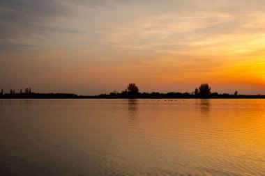 Akşamları güzel günbatımının manzarası gölün üzerinde, gölün üzerinde siluet suyun üzerinde ve bulutların sakin sularda yansıması.