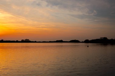 Akşamları güzel günbatımının manzarası gölün üzerinde, gölün üzerinde siluet suyun üzerinde ve bulutların sakin sularda yansıması.