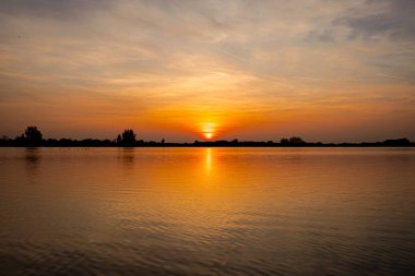 Akşamları güzel günbatımının manzarası gölün üzerinde, gölün üzerinde siluet suyun üzerinde ve bulutların sakin sularda yansıması.